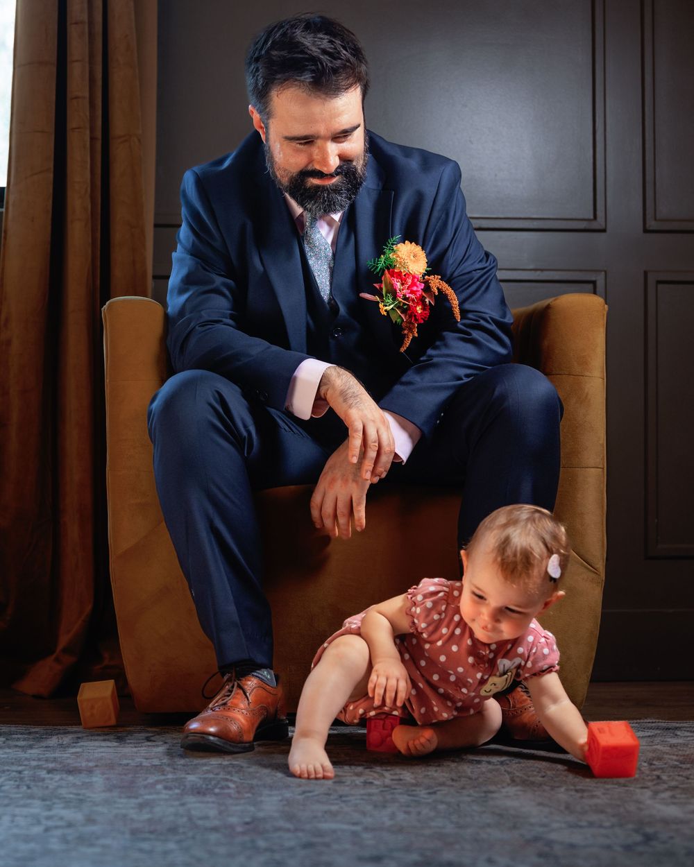 A series of four photos showing a person in a navy suit sitting on the floor playing with a small child in red clothing.