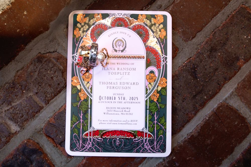Ornate decorative wedding invitation cards with floral designs and pink accents displayed on a dark textured surface.