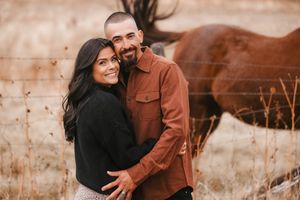Couple shares tender embrace against rustic stone wall background.