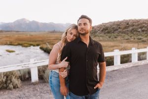 Couple poses against desert mountain backdrop on rural road with white fence.