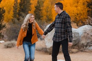 Couple playfully interacts among vibrant fall foliage and rocky terrain.