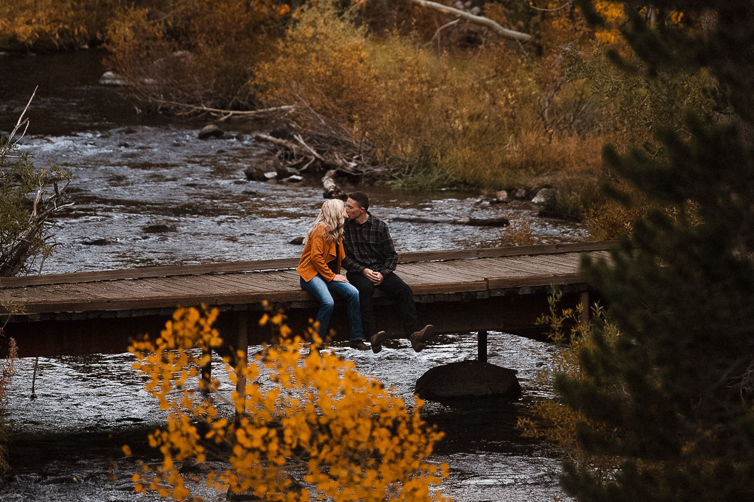 Couple sits together on fallen log surrounded by autumn foliage.