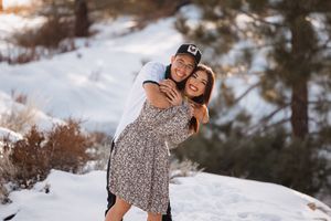 Couple embraces in snowy winter landscape with evergreen trees.