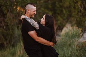 Couple embraces in golden autumn sunlight against natural outdoor backdrop.