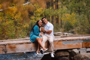 Couple sits together on wooden bench surrounded by fall foliage.