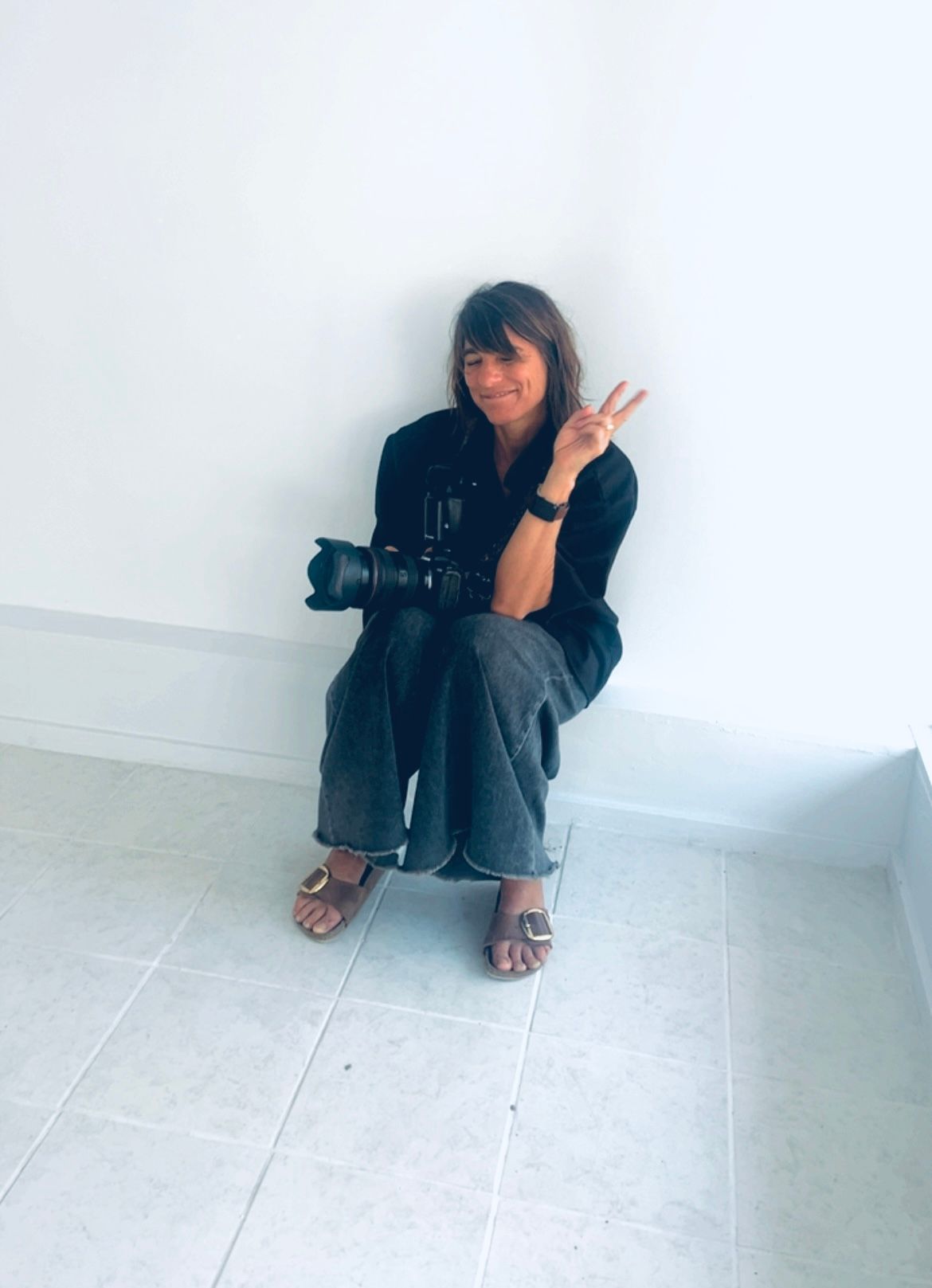 A person in black clothing sits crouched in the corner of a white room, shown in four sequential poses.