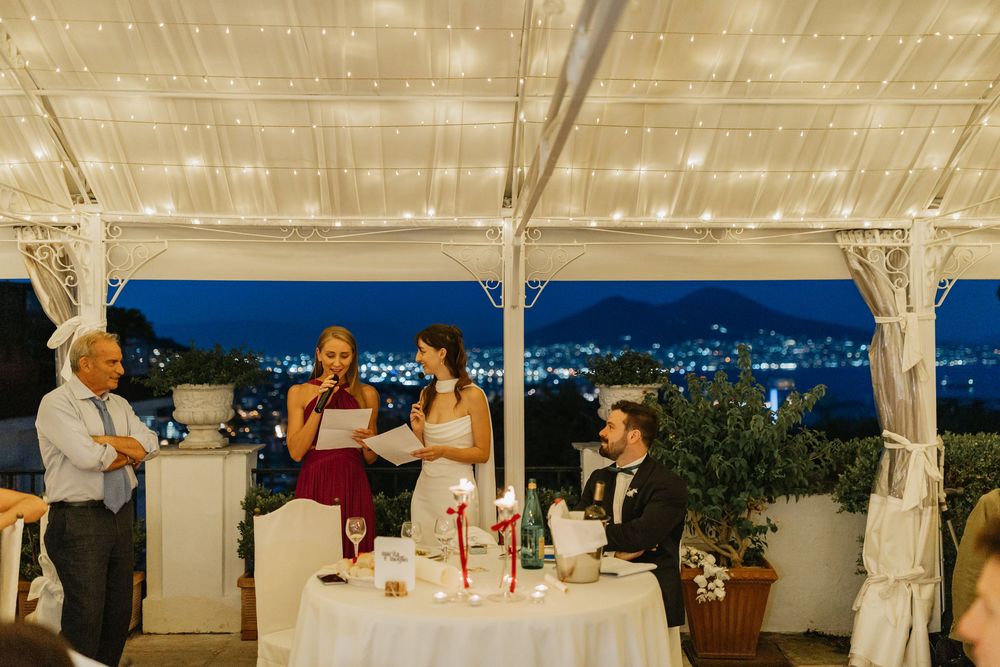 Evening celebration at an outdoor venue overlooking city lights with people gathered around a decorated table.