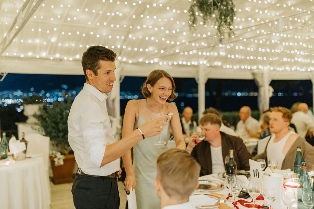 Guests gather under twinkling string lights at an outdoor evening reception, creating a warm and festive atmosphere.