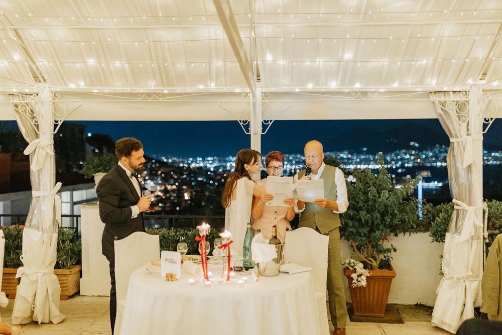 Wedding reception guests dancing and celebrating under a white tent canopy with twinkling lights at night.