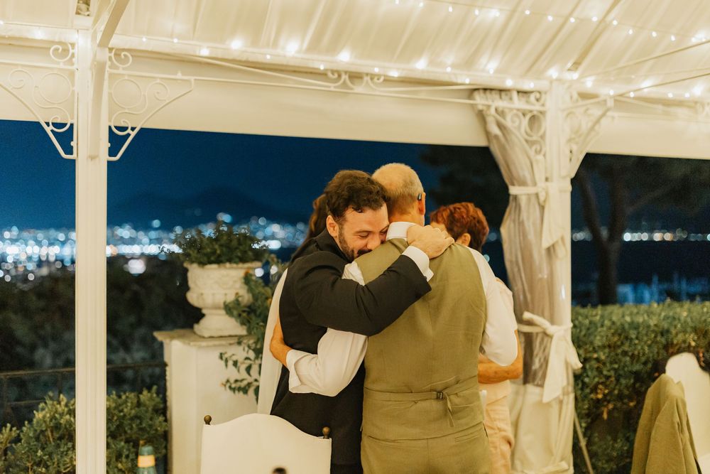 A romantic couple shares a dance under an elegant white tent at an outdoor evening wedding reception.