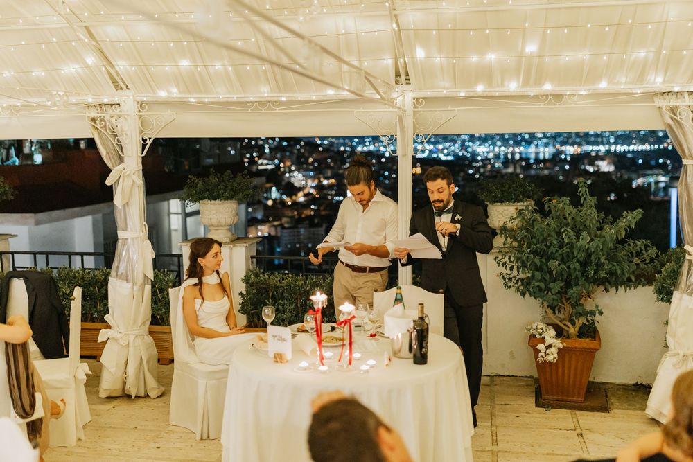 Wedding guests dance and celebrate on an illuminated dance floor under a white tent at an outdoor reception.
