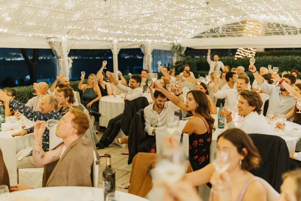 Wedding reception guests raise their hands in celebration under a white tent during an outdoor celebration.