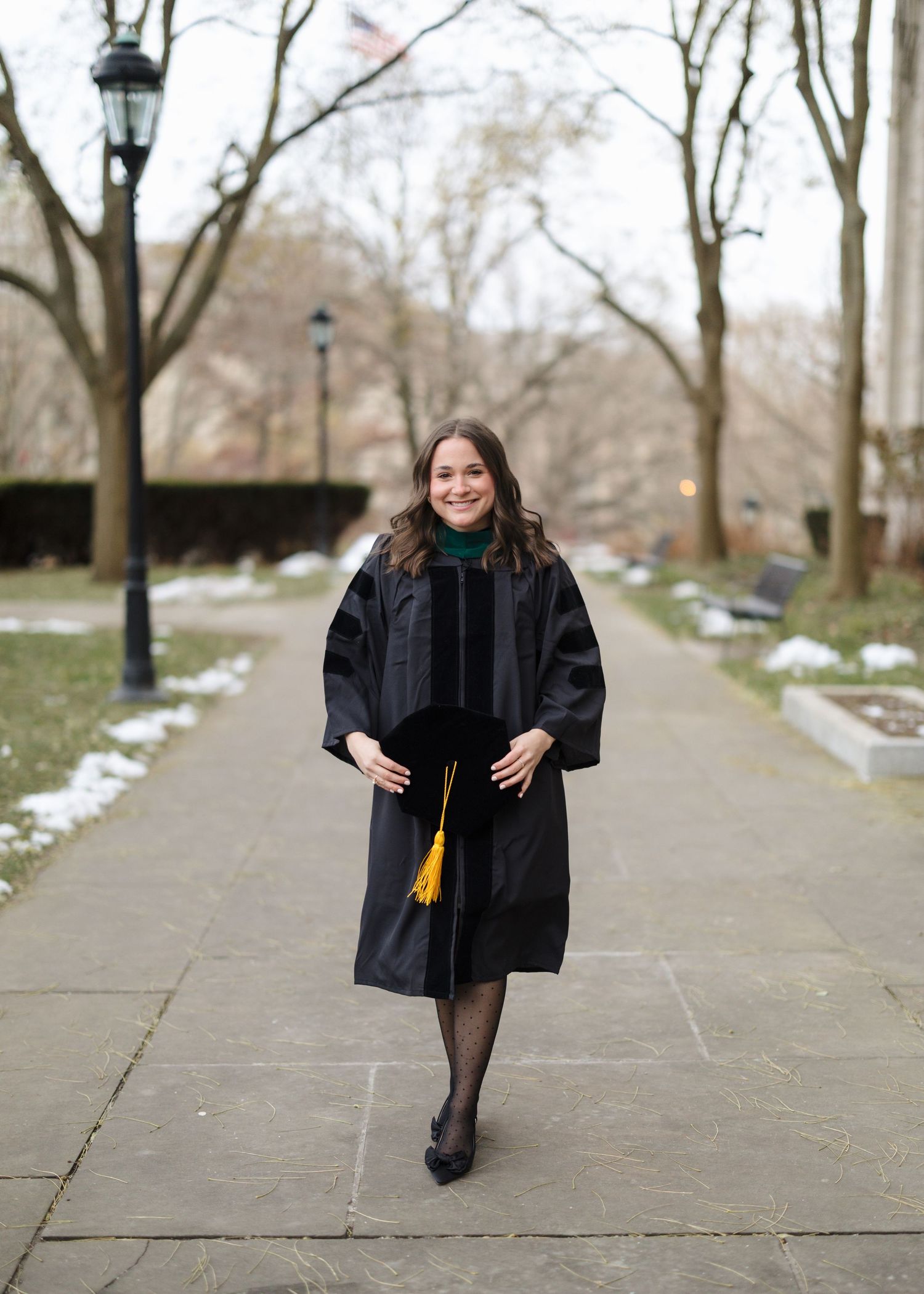 A graduation photo series showing someone in a black cap and gown walking along a snowy path with vintage lamp posts.
