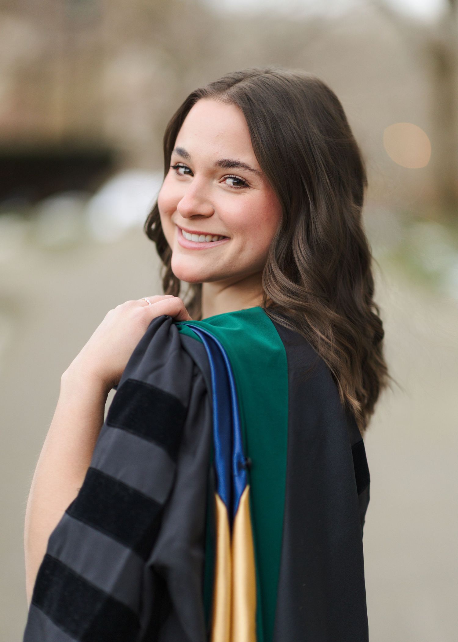 A graduate in academic regalia poses with a bright smile while wearing a green and black graduation gown and cap.