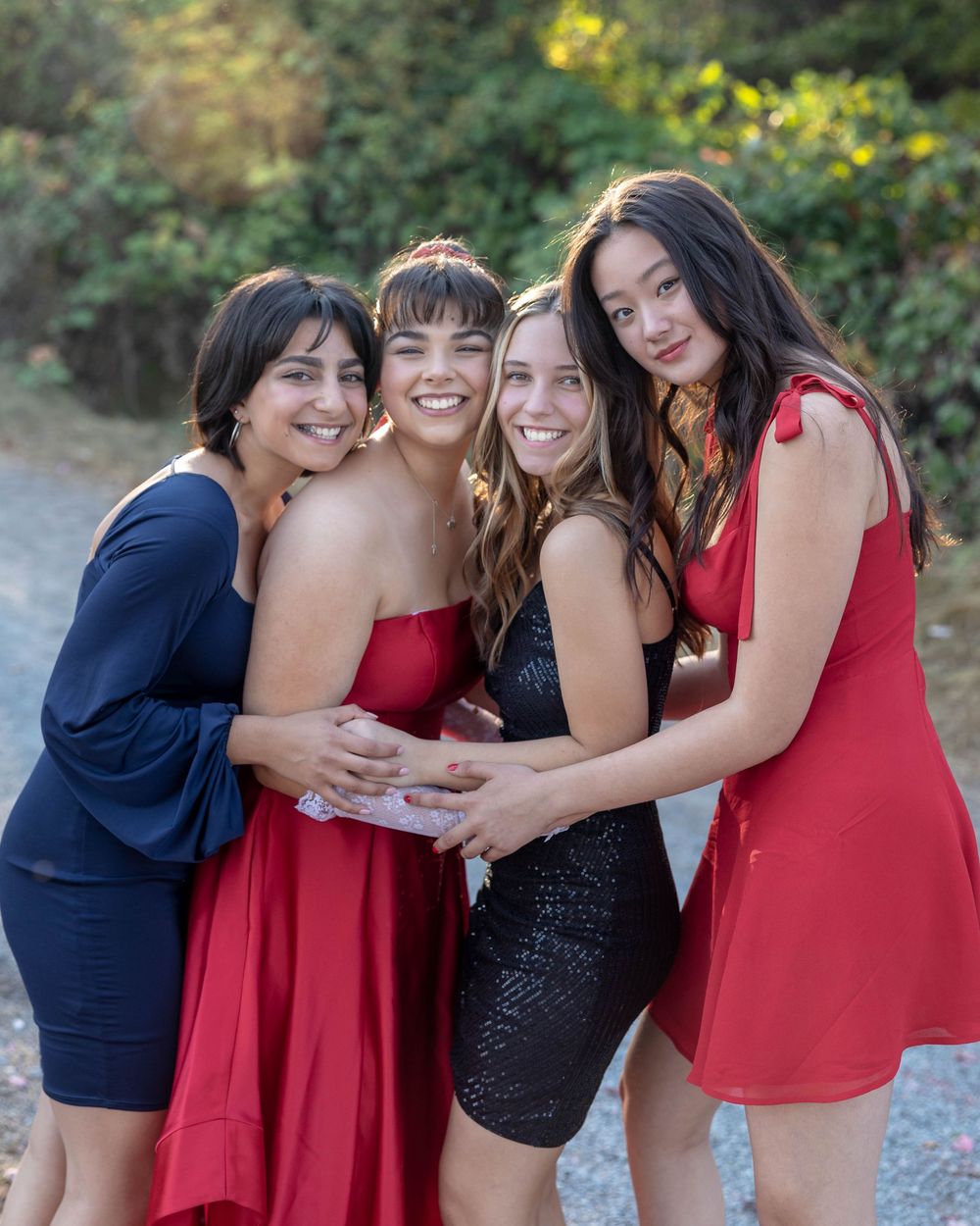 A group in red dresses and navy attire share playful moments during an outdoor photo session at dusk.