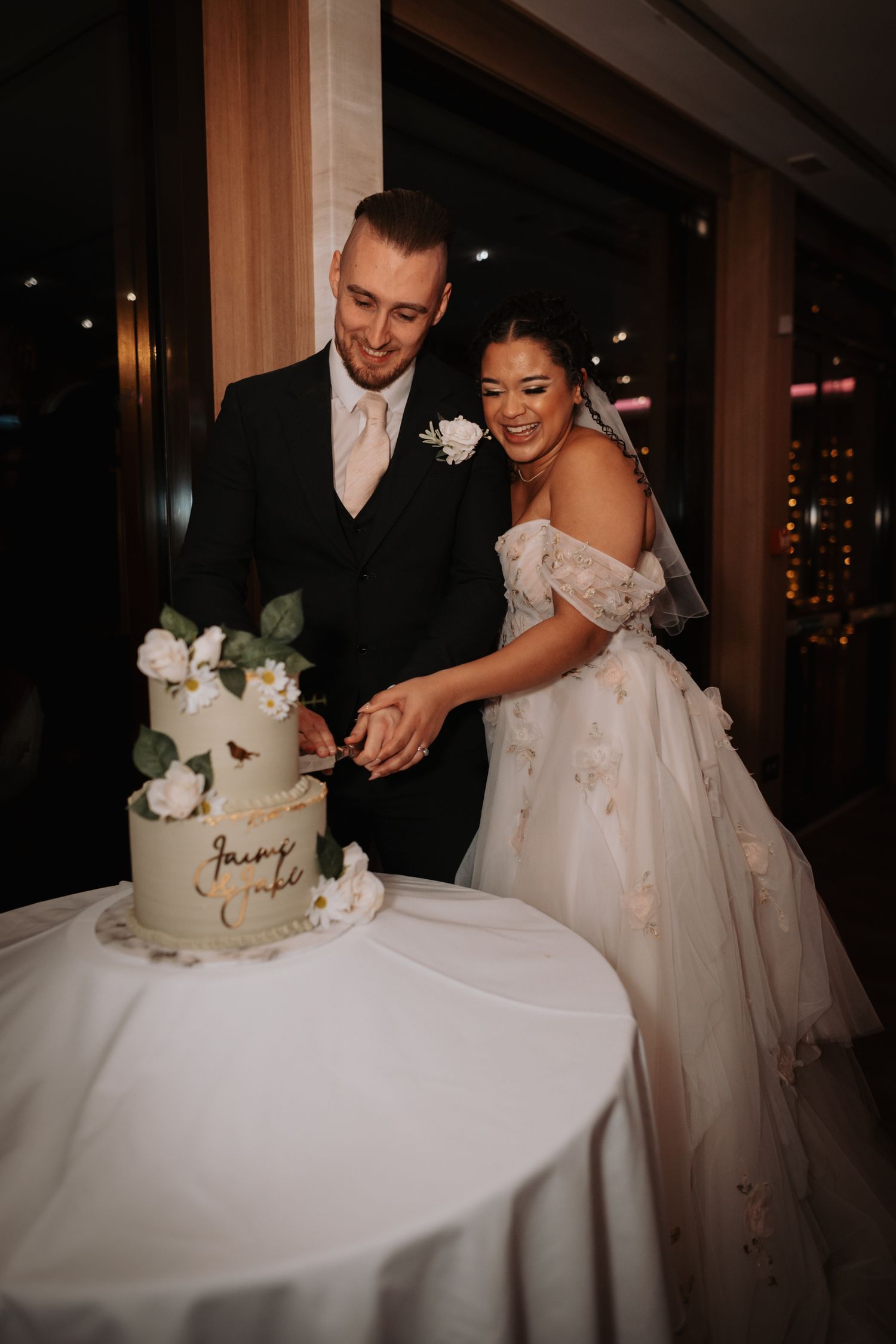 A couple in wedding attire cuts their elegant white wedding cake at an evening reception.