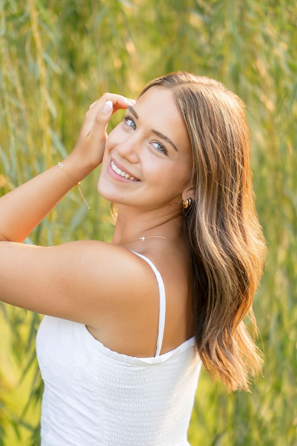 Sunlit portrait session under drooping willow branches with a white summer dress and natural backdrop.