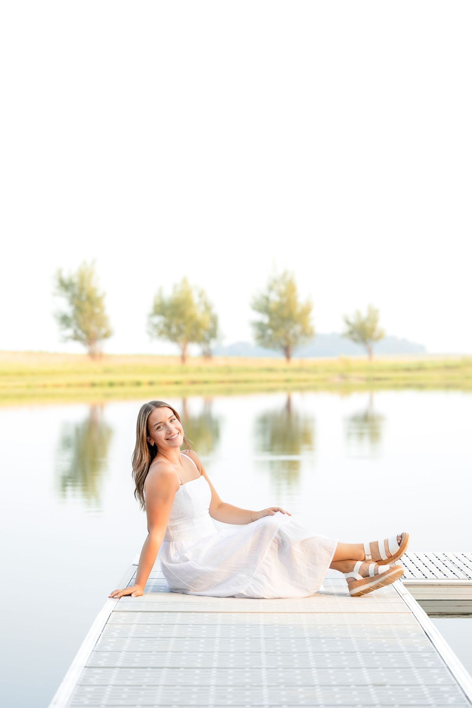 Dreamy outdoor portrait session on a white dock by a tranquil Clear Lake with trees in the background.