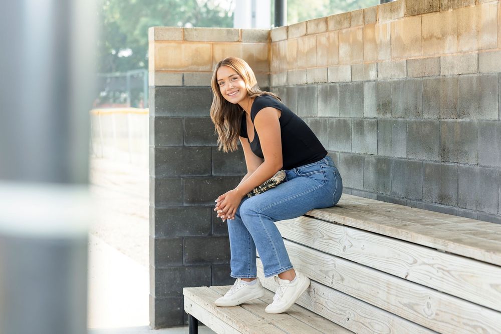 A person in jeans and white sneakers sits casually on concrete steps in an outdoor setting at the Clear Lake Iowa Softball fields.