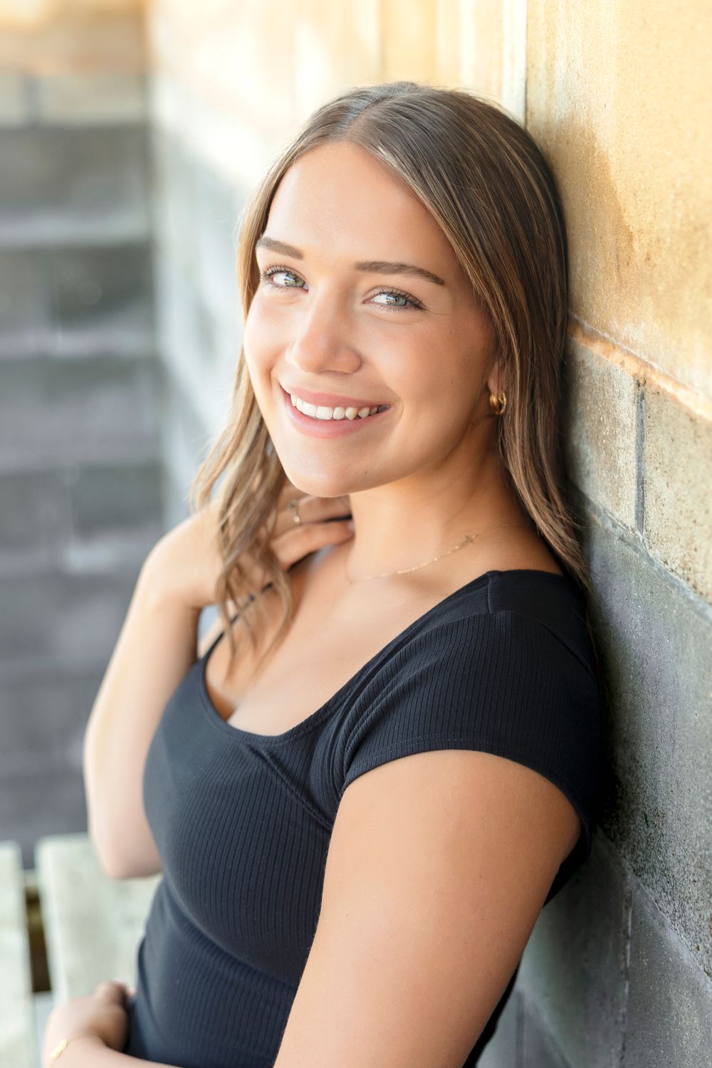 A series of outdoor portrait photos showing someone in a black top leaning against a light colored wall at Clear Lake Iowa Softball fields.
