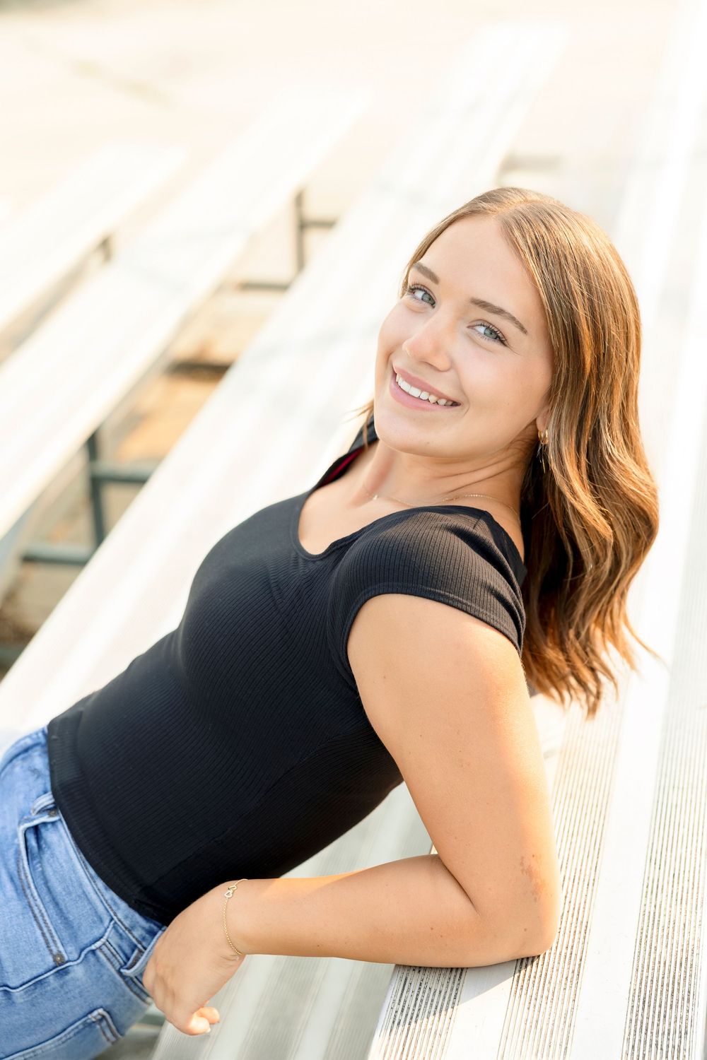 A person wearing a black top and denim jeans poses against a white architectural background in a series of senior photos at Clear Lake field