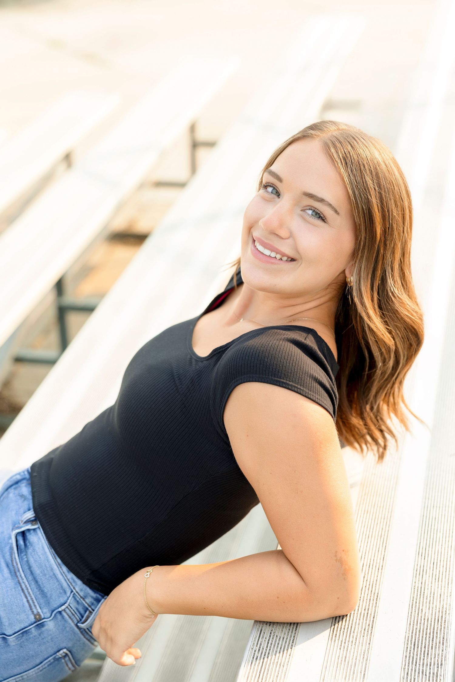 A person wearing a black top and denim jeans poses against a white architectural background in a series of senior photos at Clear Lake field