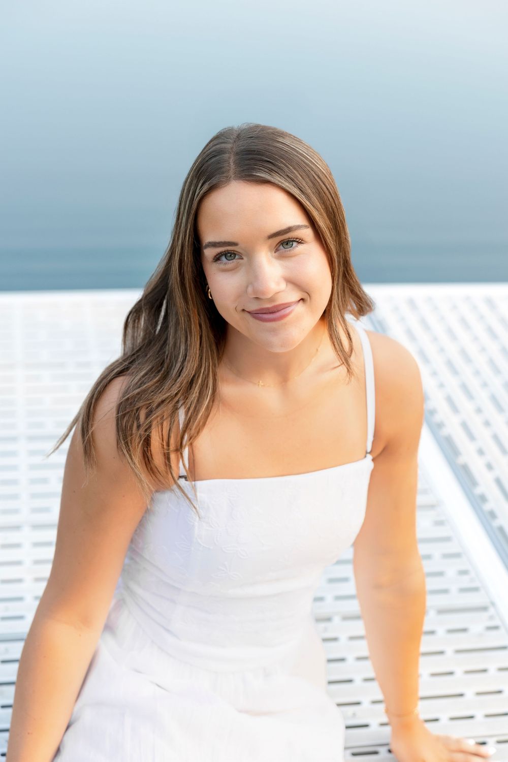 Person in white summer dress poses on a boat deck against a bright blue Clear Lake Iowa background.