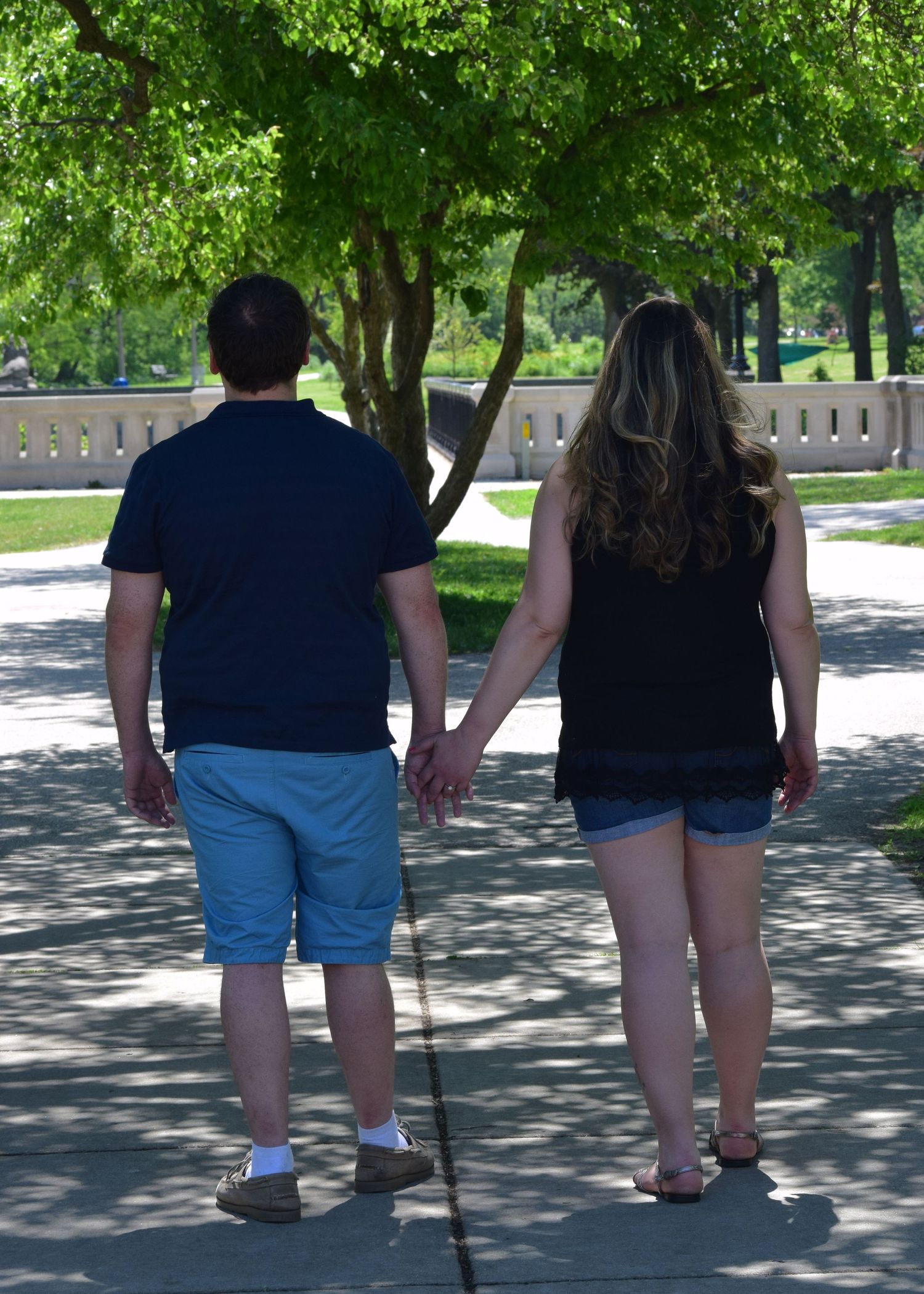 Two people walking together on a sunny path with trees casting shadows on the ground.