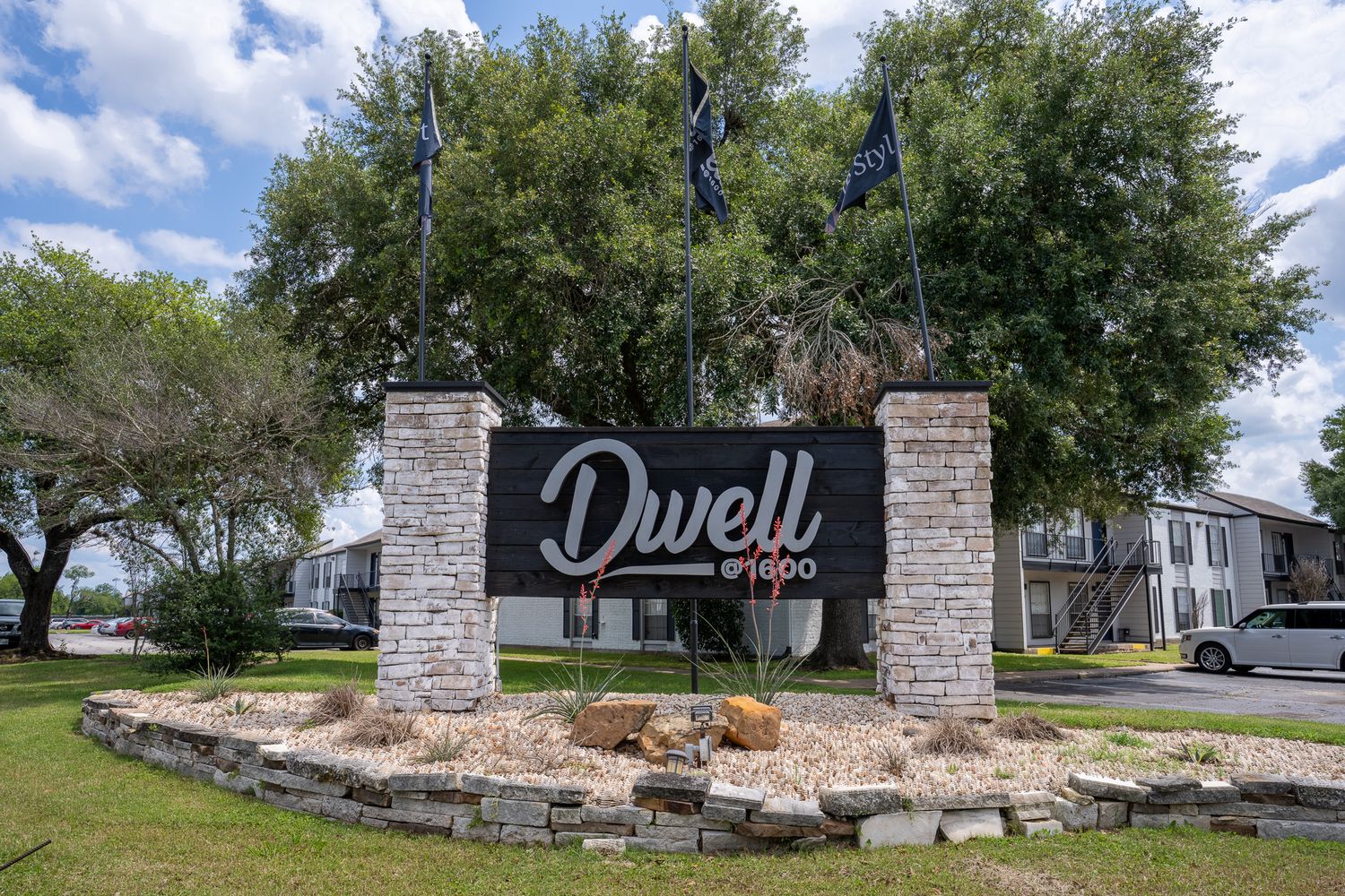 Stone entrance monument with landscaping welcomes visitors to residential neighborhood on sunny day.