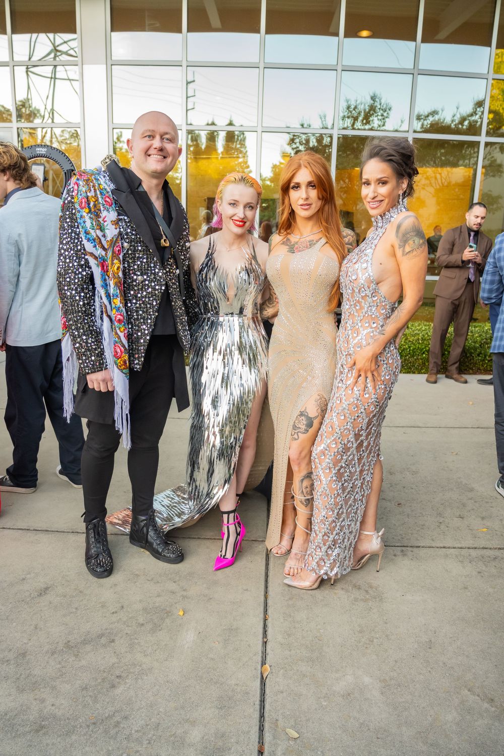 A group of people at a formal event wearing sparkly dresses and evening attire stand together outside.