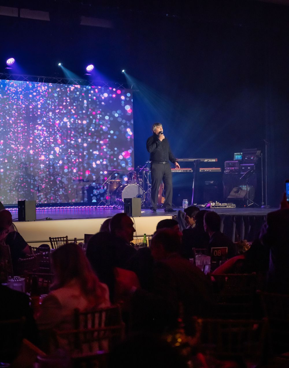 A performer on stage with colorful lights and projection screens during a nighttime concert performance.