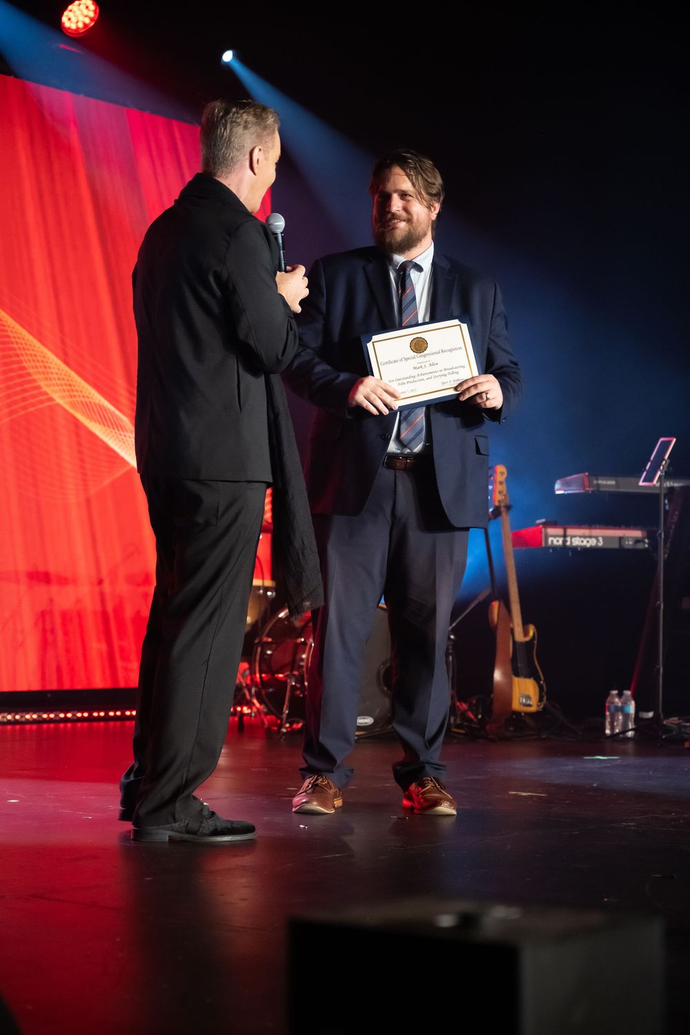 Award ceremony on stage with dramatic red and blue lighting during formal presentation event.