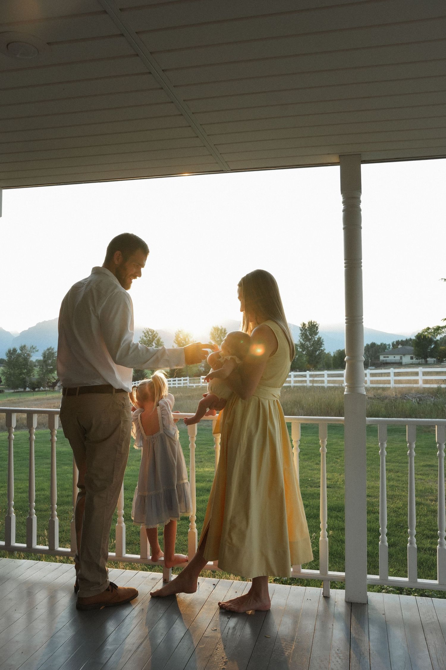 People gather on a covered porch at sunset overlooking a fenced pasture with golden sunlight streaming through.