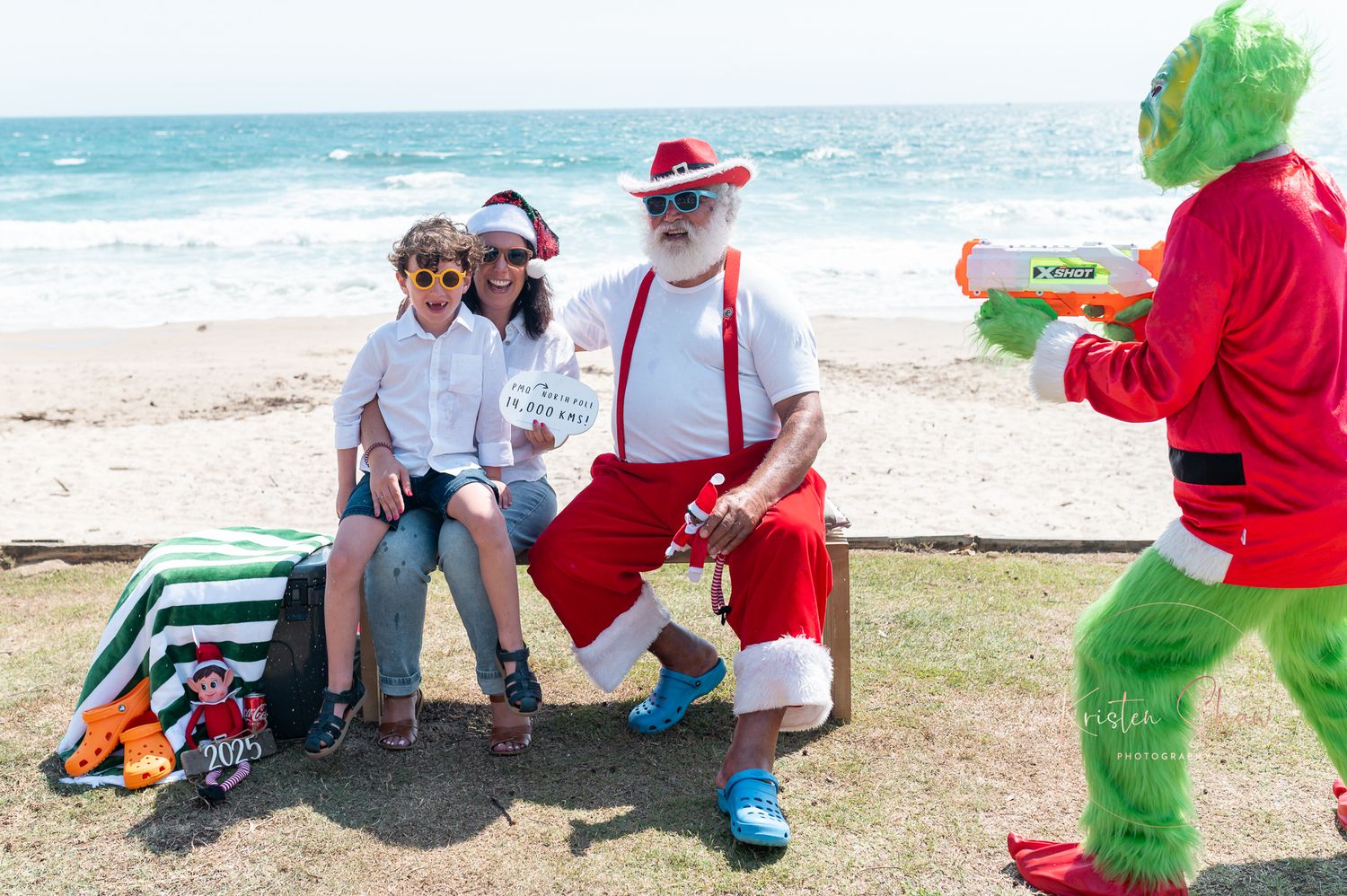 Group of people enjoying a festive holiday gathering on a beach with red and white Christmas decorations.
