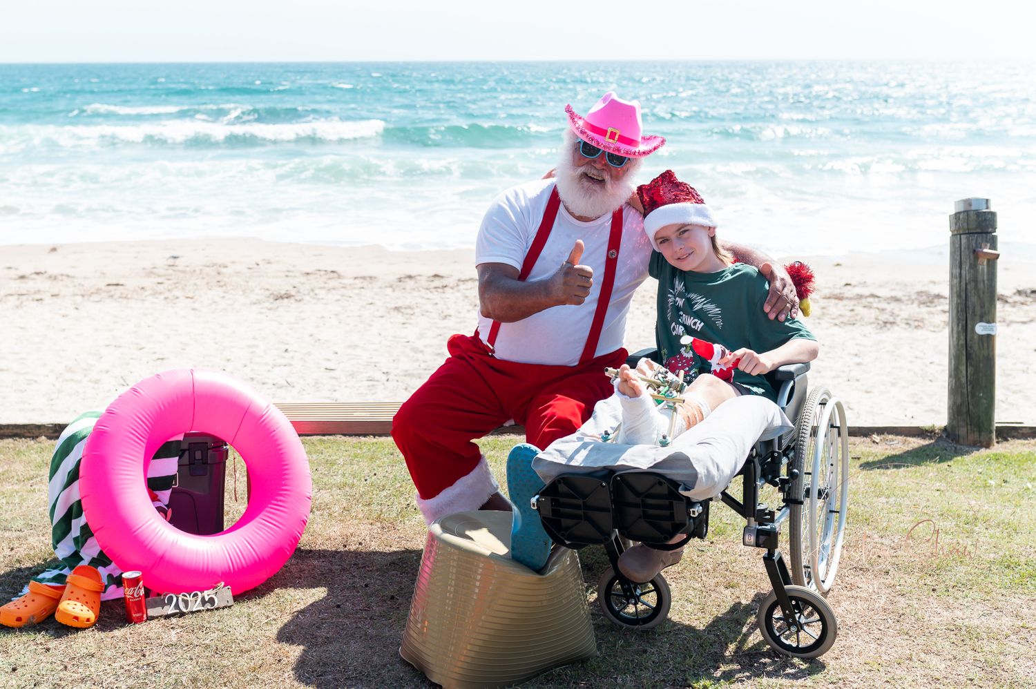 Beachgoers in wheelchairs enjoying accessible beach activities with pink flotation devices and mobility assistance equipment.