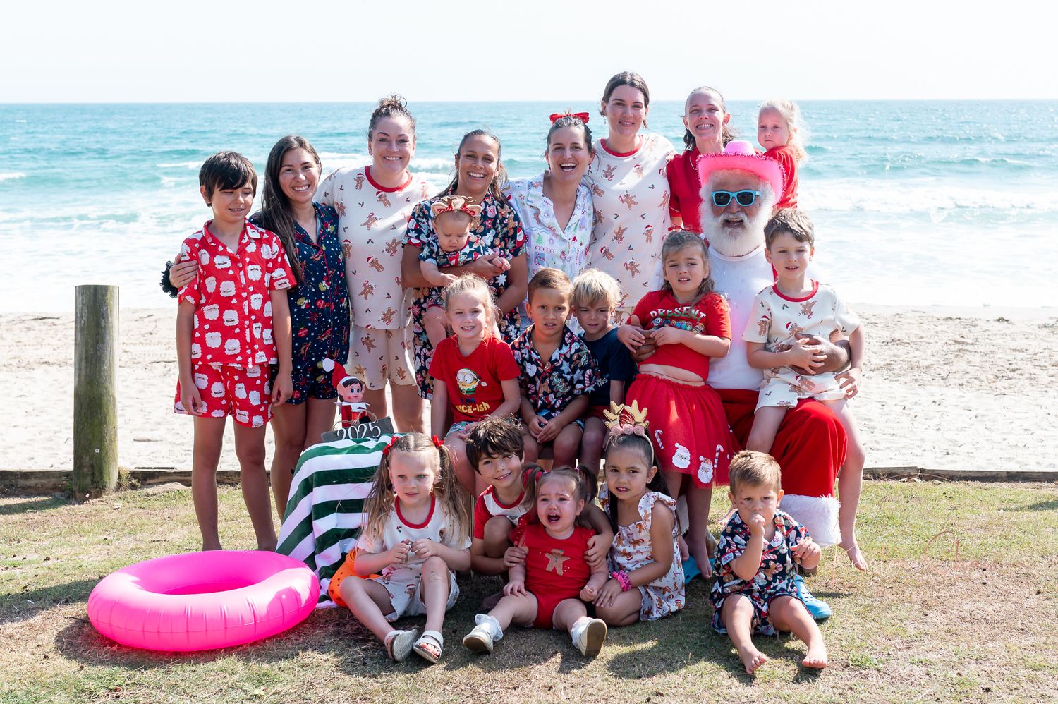 A group wearing festive red and white outfits poses together on the beach for holiday photos.
