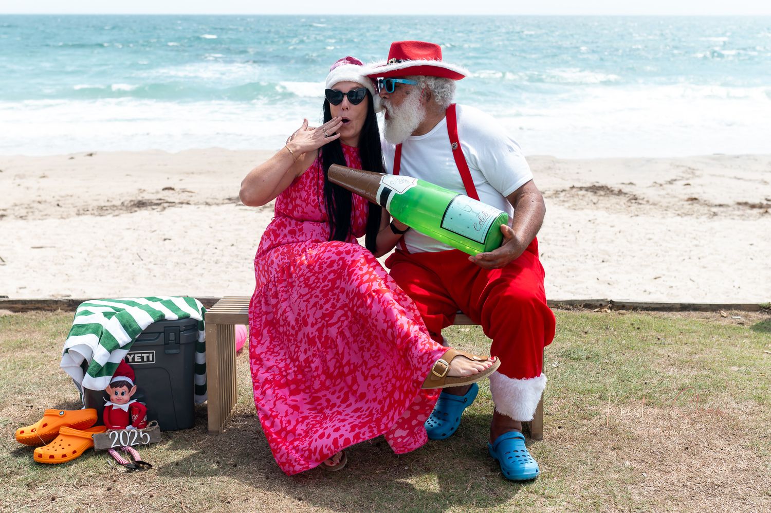 A person in a pink dress sits on a beach with a drink while enjoying the ocean view.