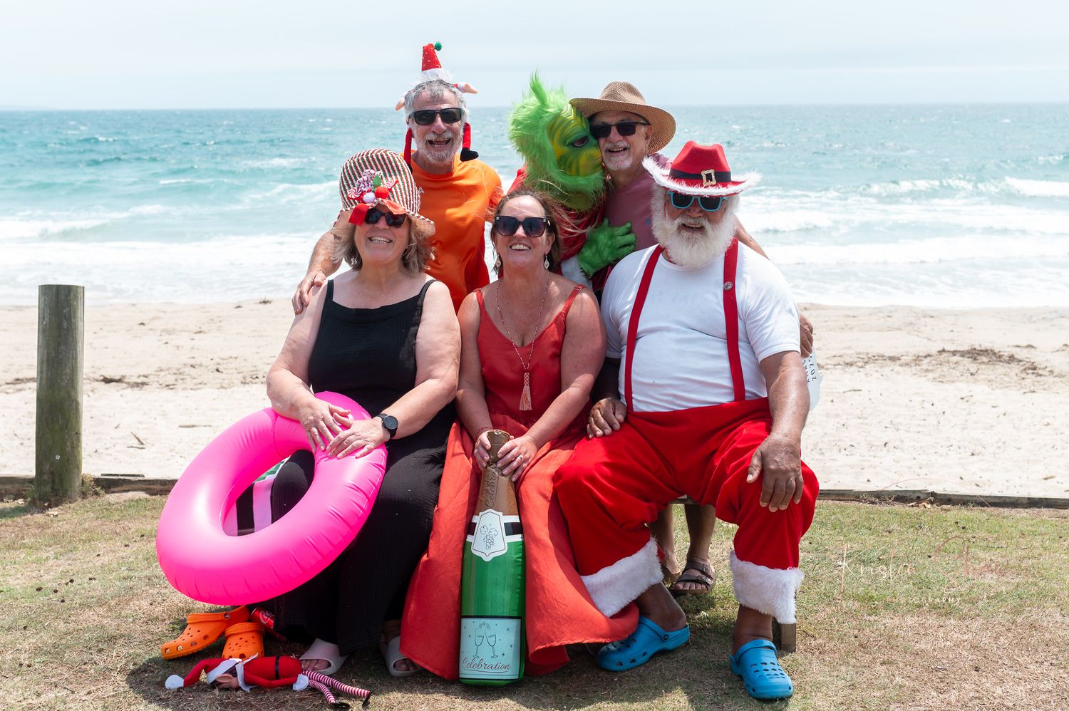 Group relaxing on beach with colorful inflatable float and festive holiday attire.