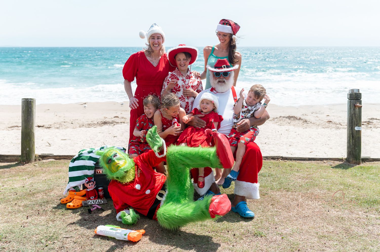 Group in festive holiday attire gathered at a sunny beach location for Christmas celebrations.
