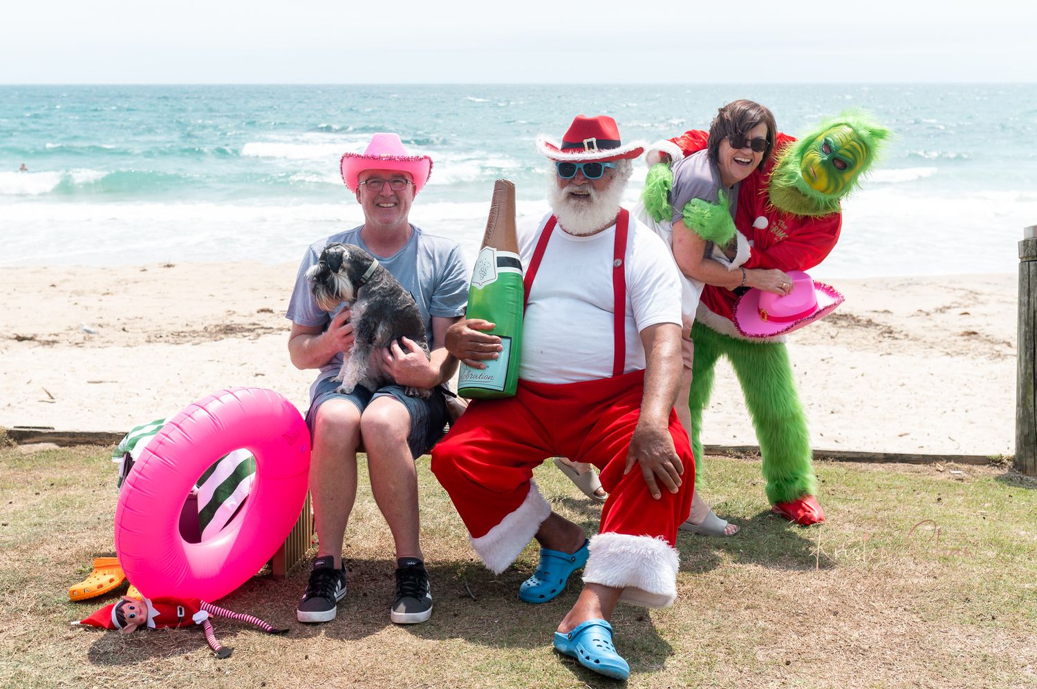 A festive group in colorful costumes with beach accessories including a pink float ring poses by the ocean.