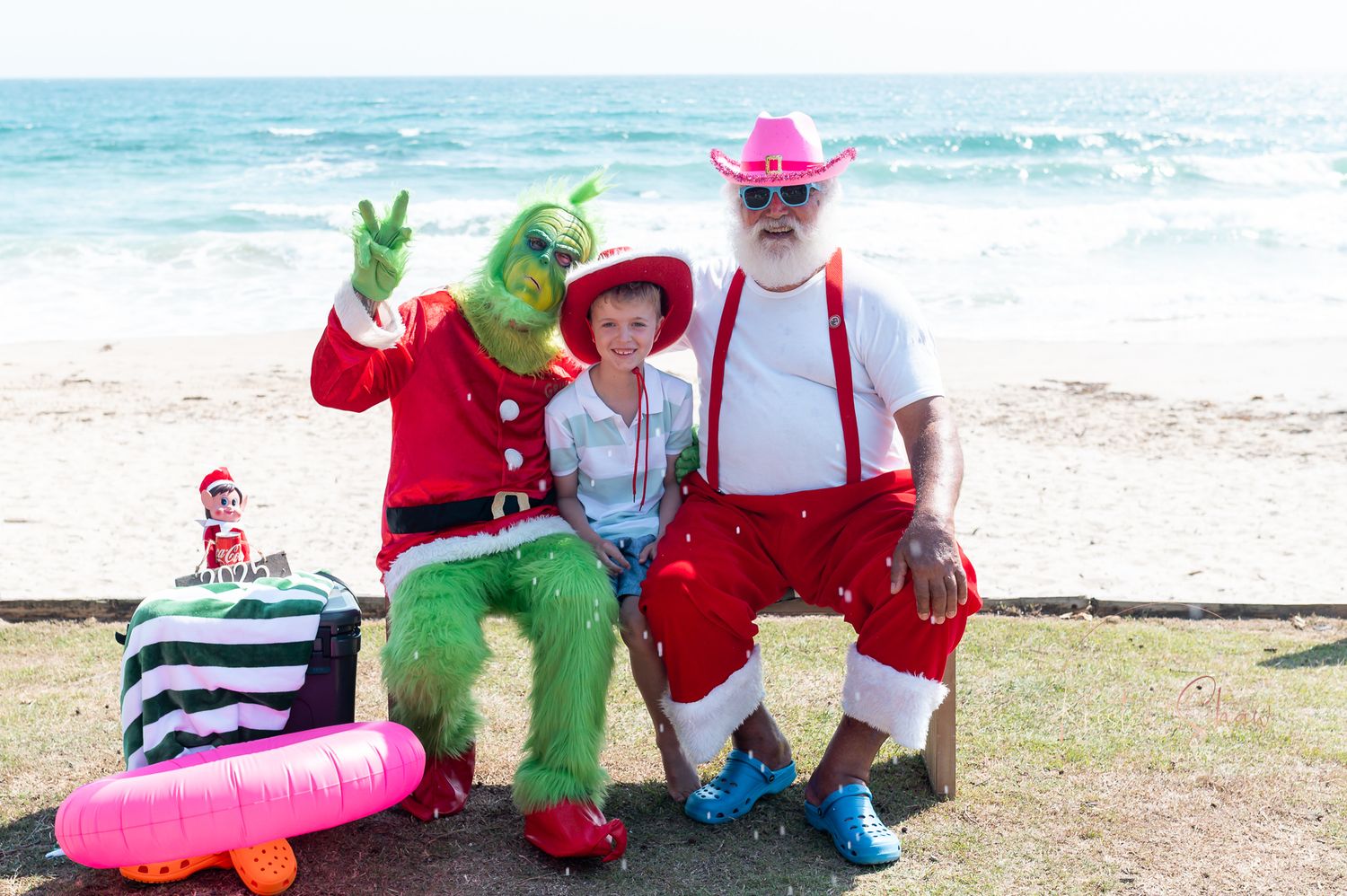 A group of people in colorful outfits and costumes pose together at a beach with inflatable toys.