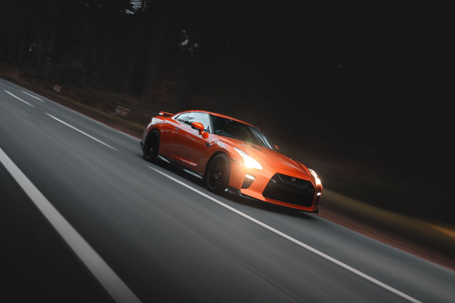 Orange sports cars racing on dark track with dramatic lighting and motion blur.
