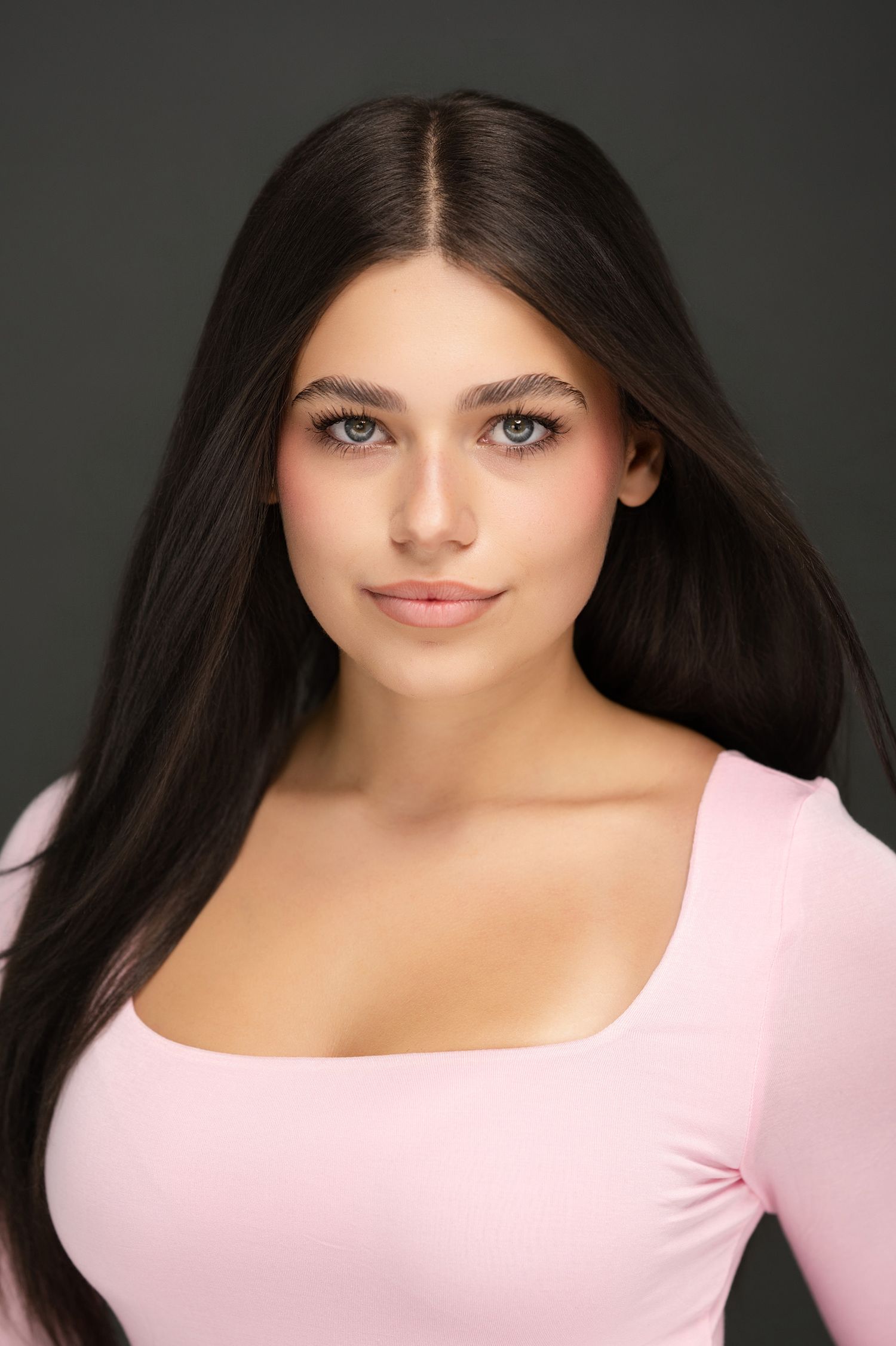 Portrait of person with dark hair wearing pink top against dark background.