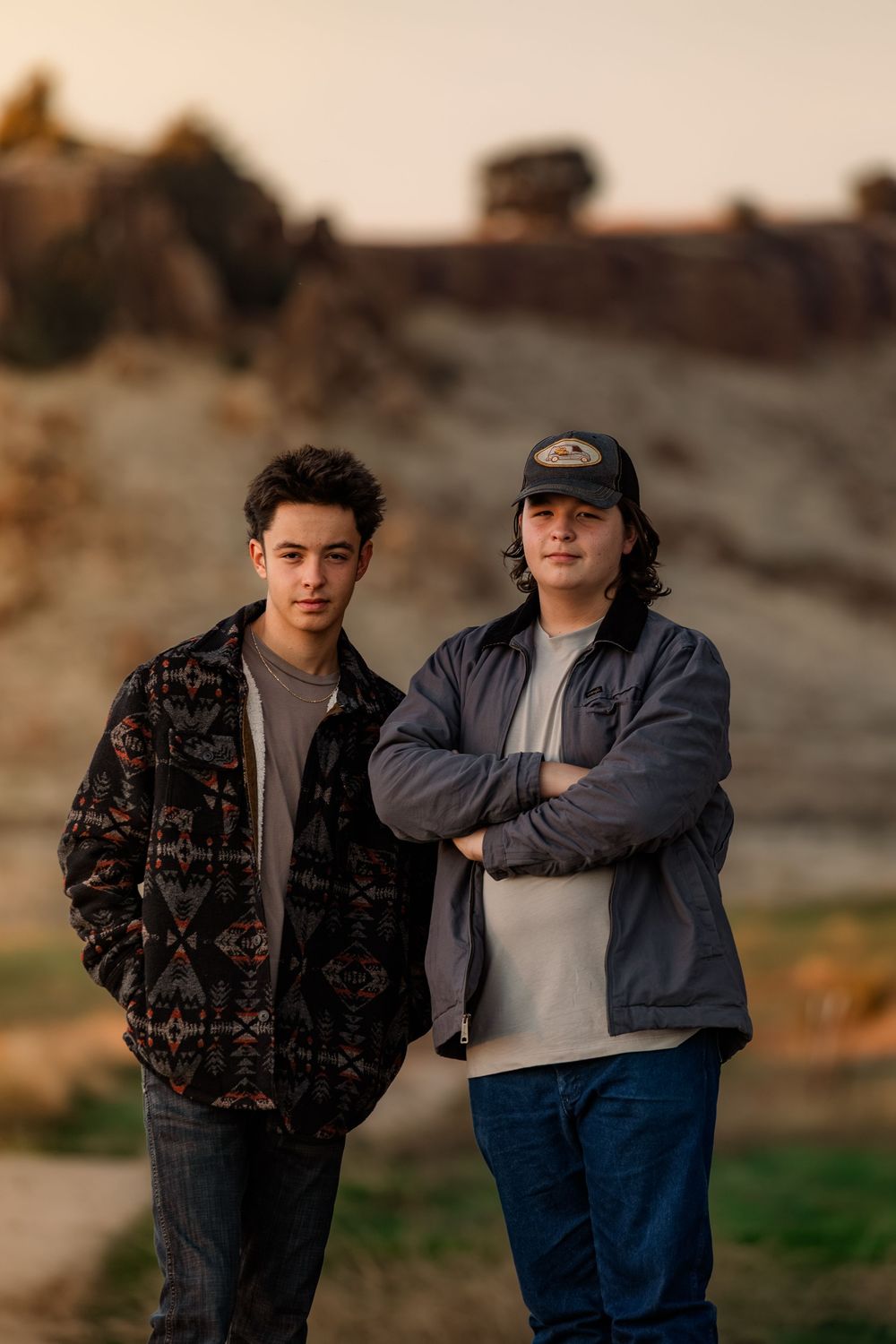 Two people stand together in casual clothing against a scenic outdoor backdrop during golden hour.