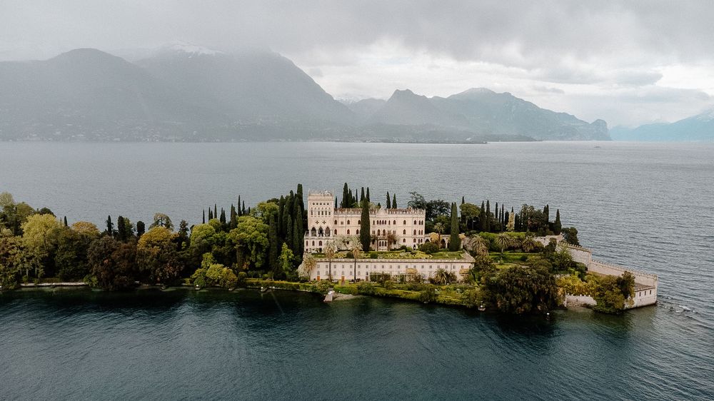 Panoramic view of Lake Garda in Italy showing historic villas and cypress trees along the misty shoreline.