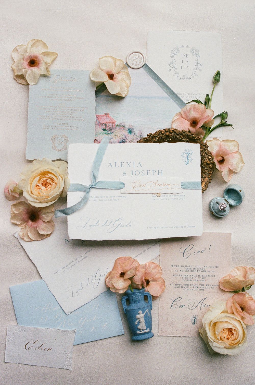 Elegant wedding stationery suite in soft blue and white with peach roses and vintage blue jar on light background.
