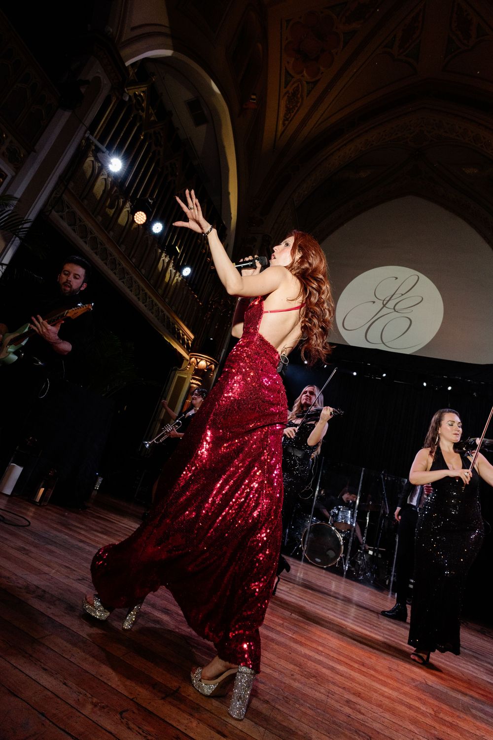 A woman in a red sequin gown dances elegantly at a formal event with a live band performing in the background.