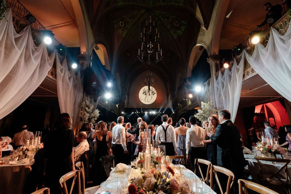 Elegant wedding reception in a grand cathedral venue with draped fabric, candlelit tables, and guests mingling on the dance floor.