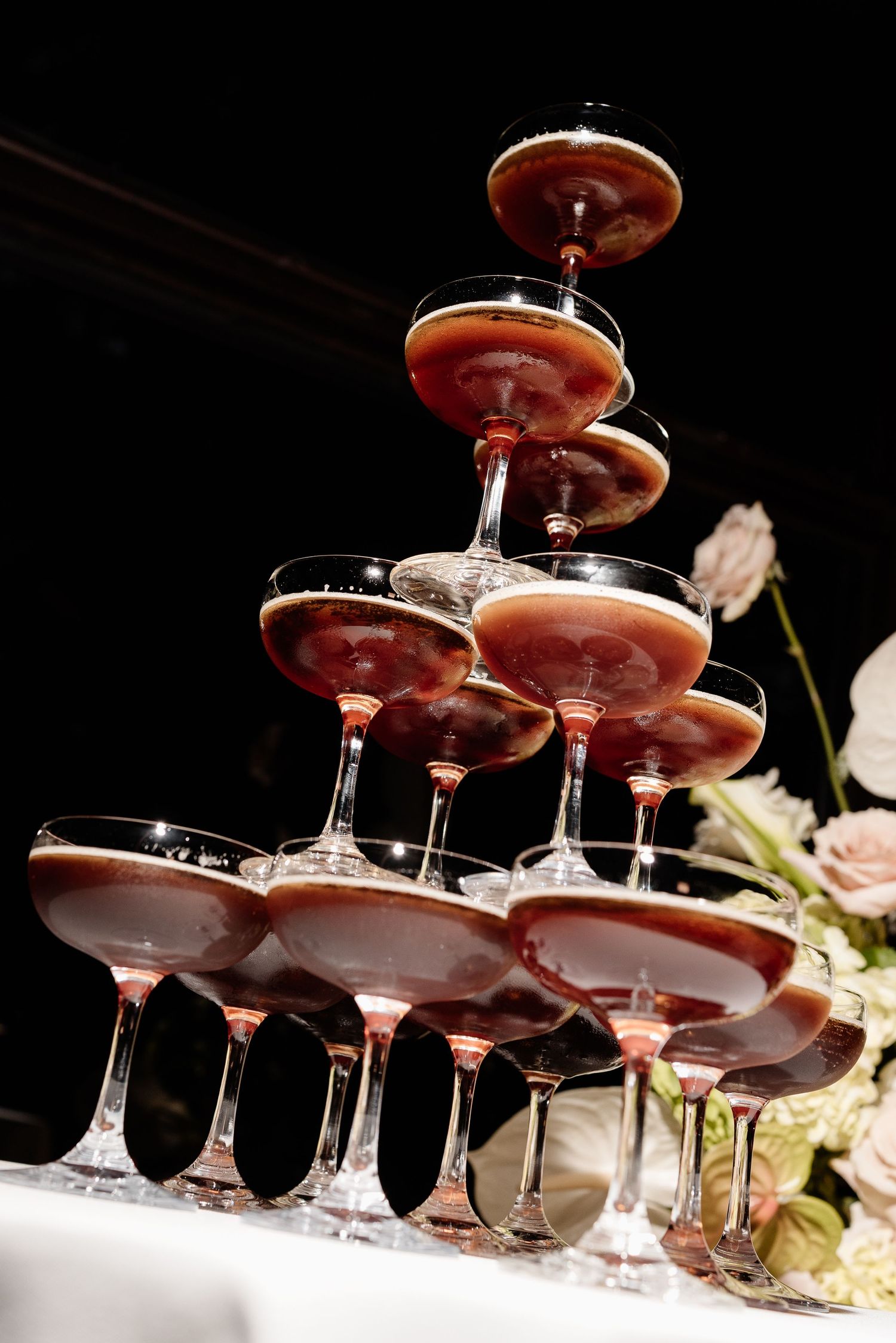 Elegant champagne tower with pink rosé filled coupe glasses stacked in pyramid formation at a formal event.