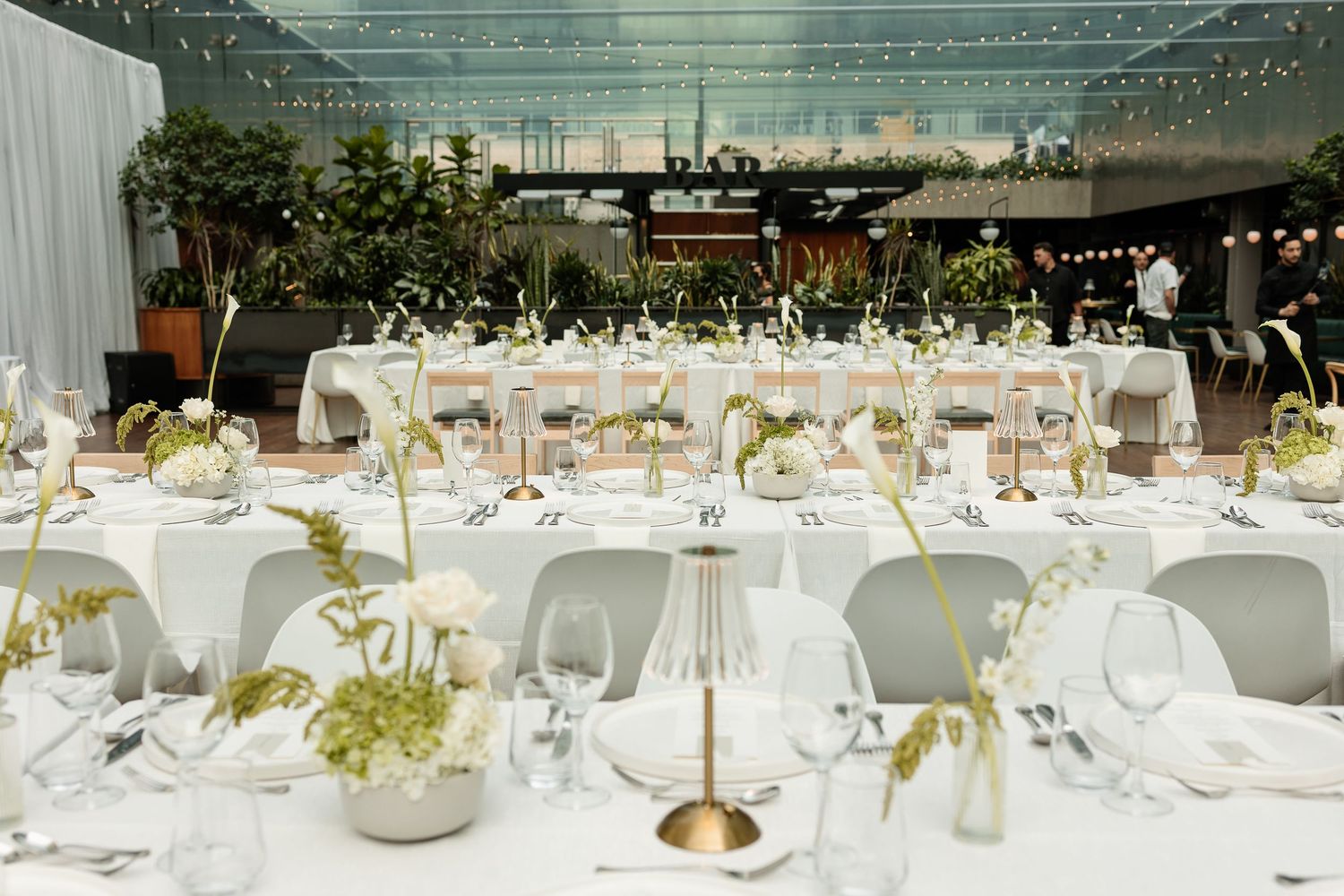 Elegant white wedding reception tables decorated with floral centerpieces and gold accents in a banquet hall setting.